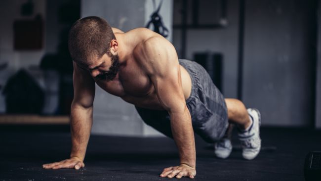 Topless man getting ready to perform a full push up on the gym floor