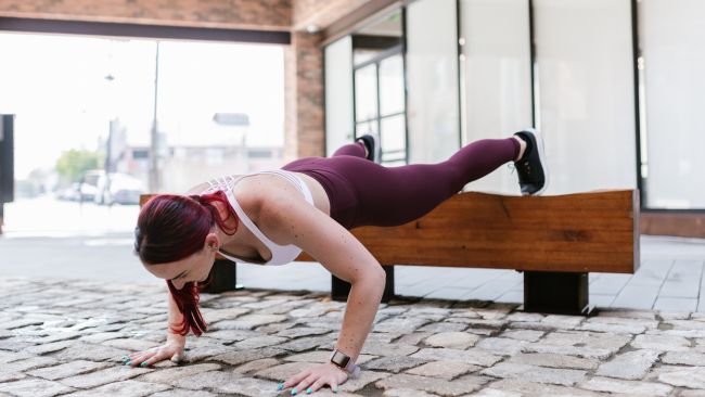 Woman performing incline push ups with her feet elevated on a wooden bench